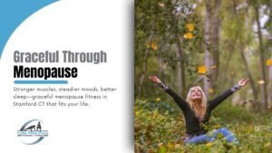 50+ smiling with arms raised among falling autumn leaves, symbolizing graceful menopause fitness in Stamford CT.