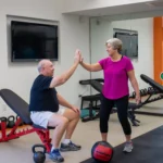 An older man and woman high-fiving in a gym setting