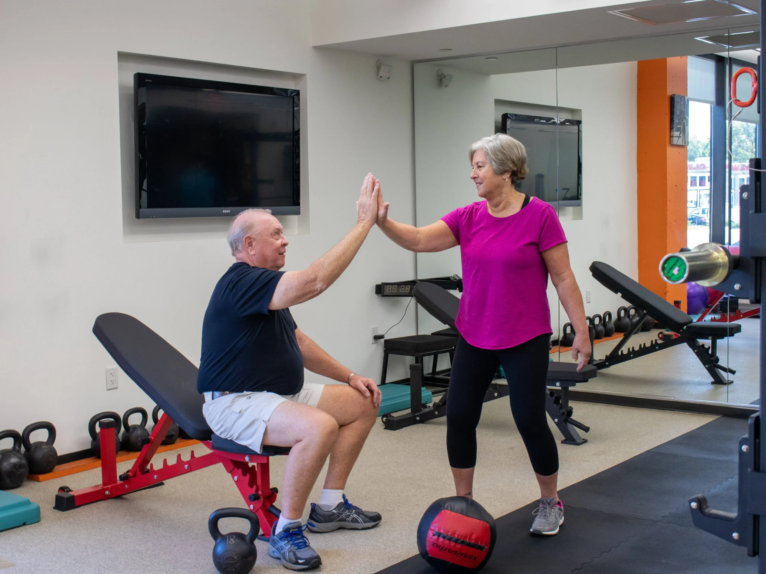 An older man and woman high-fiving in a gym setting